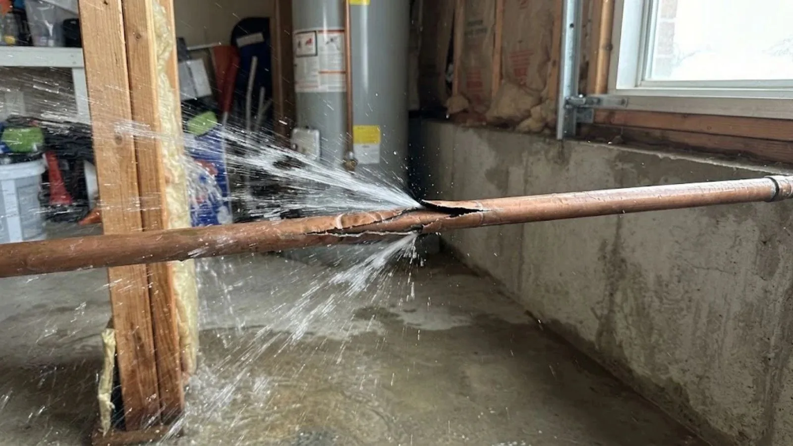 Burst copper pipe spraying water across a basement wall